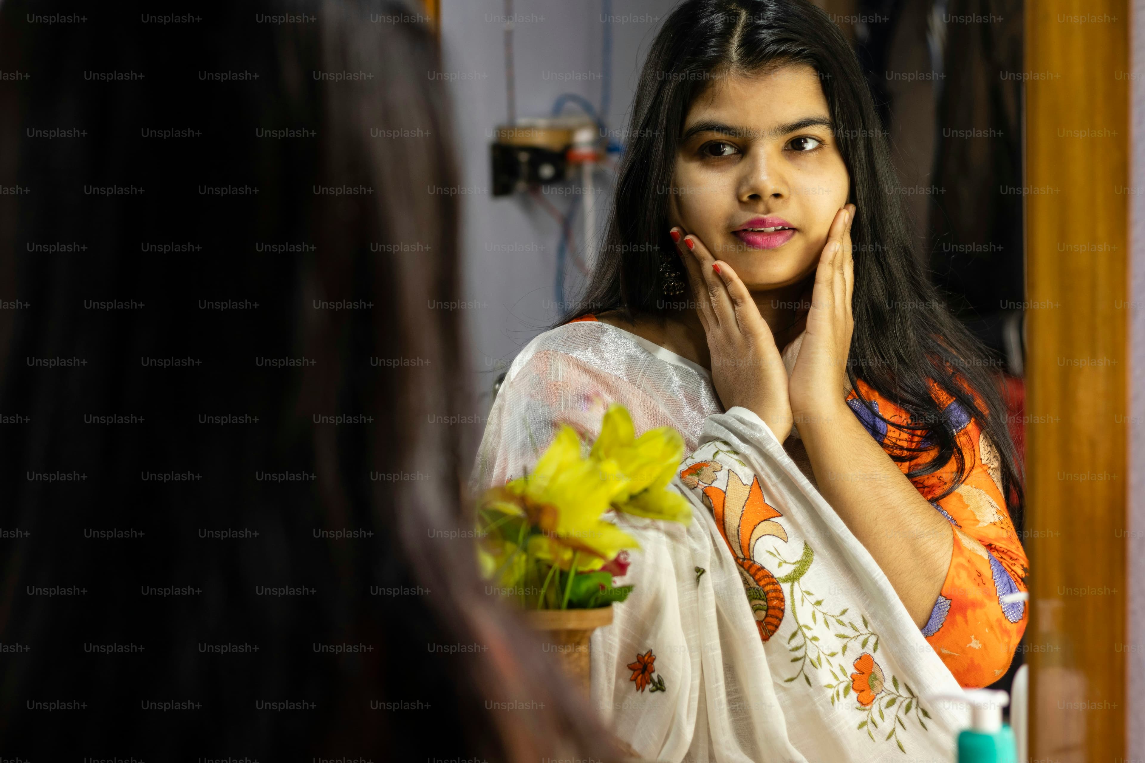 A South Asian woman examining her face in a mirror